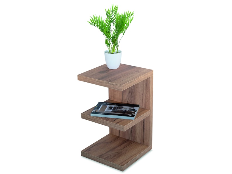 Puede incluir: Una mesa auxiliar de madera con tres estantes. El estante superior tiene una peque&ntilde;a planta en maceta con hojas verdes. El estante del medio tiene un libro encima. La mesa es marr&oacute;n y tiene un dise&ntilde;o moderno.