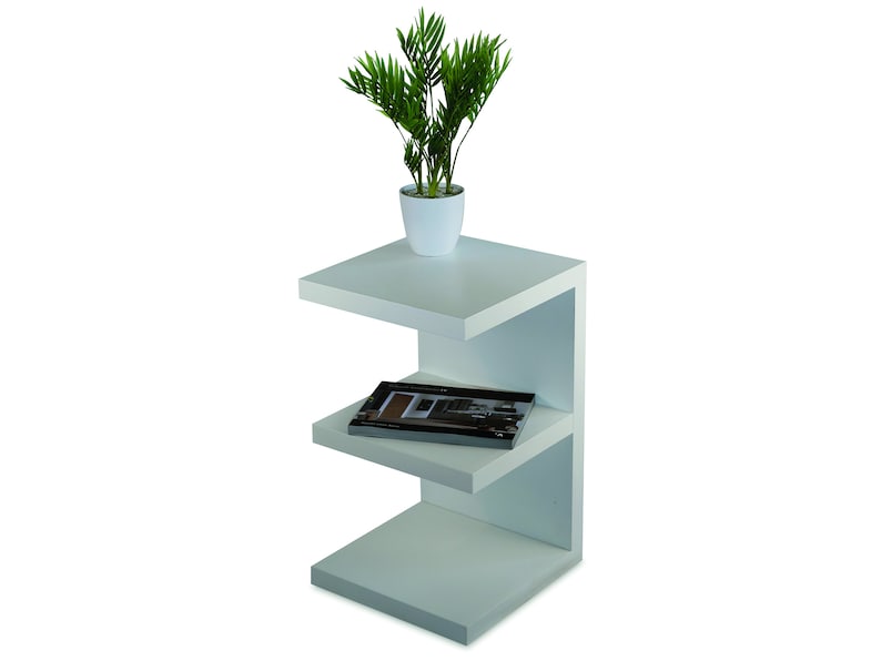 Puede incluir: Mesa auxiliar blanca con tres estantes. El estante superior tiene una planta en maceta con hojas verdes. El estante del medio tiene un libro. La mesa est&aacute; hecha de madera y tiene un dise&ntilde;o moderno.
