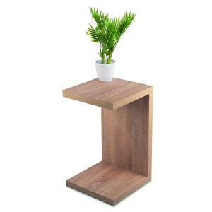May include: A light brown wooden side table with a shelf. The table has a square top and a curved front. A small potted plant with green leaves is on the top of the table.