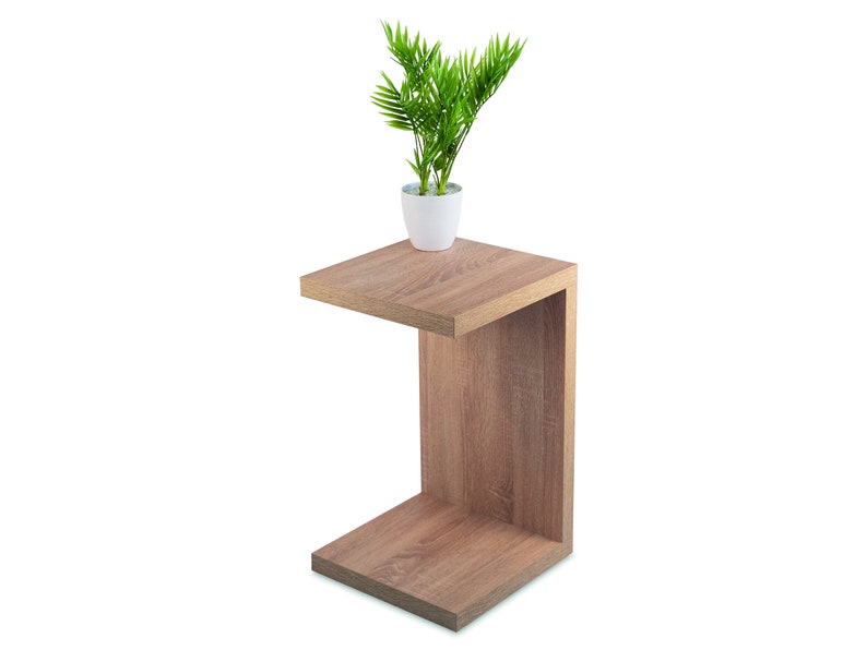May include: A light brown wooden side table with a shelf. The table has a square top and a curved front. A small potted plant with green leaves is on the top of the table.