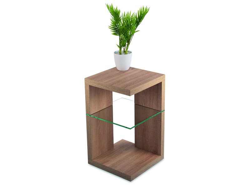 May include: A light brown wooden end table with a glass shelf. The table has a square top and a rectangular base. A small potted plant is on the top shelf.