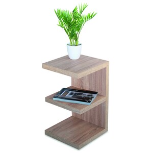 Puede incluir: Una mesa auxiliar de madera marr&oacute;n claro con tres estantes. El estante superior tiene una peque&ntilde;a maceta blanca con una planta verde. Un libro est&aacute; en el estante del medio.