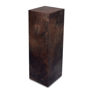 Op de afbeelding: Een hoog, rechthoekig voetstuk gemaakt van donkerbruin materiaal met een getextureerd, gevlekt oppervlak. Het voetstuk is een massief stuk zonder zichtbare naden of voegen.