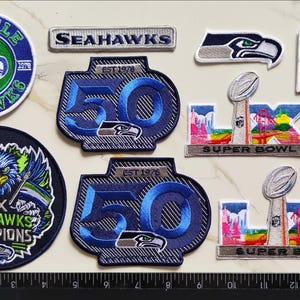 Op de afbeelding: Een verzameling geborduurde Seattle Seahawks en Super Bowl patches, inclusief ronde teamlogo's, 50-jarig jubileumemblemen, een teamnaamstrip, een vogelkoplogo, een Amerikaanse vlag, een NFL-schild en twee Super Bowl LX trofee-patches.
