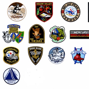 May include: A collection of twenty-two embroidered patches featuring various designs, including logos for Hamm's, Squaw Valley, Ski Jay Peak, Shellback, Pacific Beach Surf Shop, Special Forces, The Duke, Mercury Racing, Loch Birch, Vail, Pittsburgh Police, Rhode Island State Police, Dodgers, Vermont, Blue Knob Ski Area, Evinrude, and Resort East.
