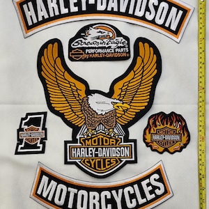 May include: A selection of Harley-Davidson patches. The patches display the Harley-Davidson logo, eagle designs, and the words "Motorcycles" and "Cycles." The patches are black, orange, and white.