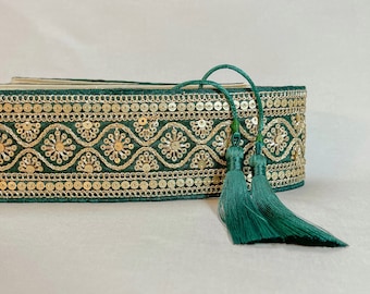 Può includere: Finitura in tessuto verde con paillettes dorate e un fiocco verde. La finitura presenta un motivo ripetitivo di piccoli cerchi e una linea ondulata.