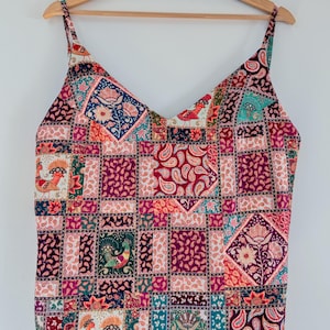 May include: A sleeveless top with a patchwork design featuring a variety of colors and patterns, including paisley, floral, and geometric designs. The top has a V-neckline and thin straps.