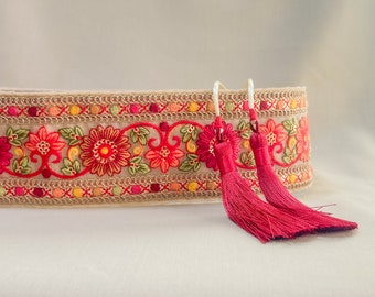 Può includere: Un bordino in tessuto beige con ricamo floreale rosso, arancione e giallo e due nappine rosse.