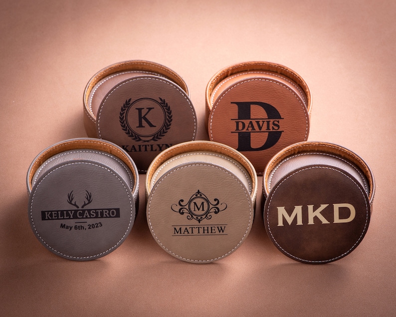 May include: Six round leather coasters with personalized engravings. The coasters are brown, gray, and beige. The engravings include names, initials, and dates.