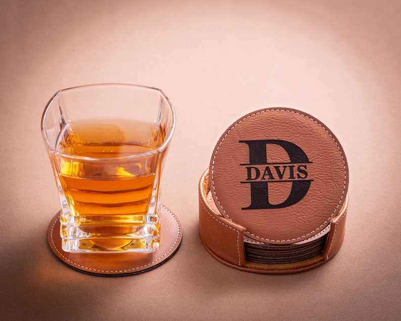 May include: Set of six brown leather coasters with a personalized initial and name "DAVIS" in black lettering. The coasters are stacked and displayed with a glass of amber liquid on a matching coaster.