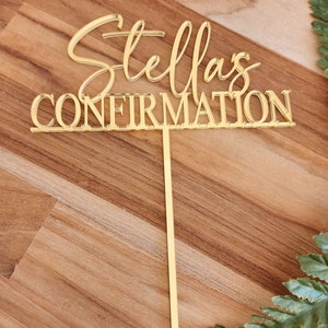 May include: Gold cake topper with the text "Stella's Confirmation" in a cursive font.