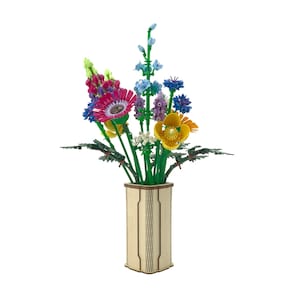 May include: A colorful bouquet of artificial flowers in a light-colored wooden vase. The arrangement includes various blooms in shades of pink, blue, yellow, and purple, with green stems and leaves. The vase has a rectangular shape.