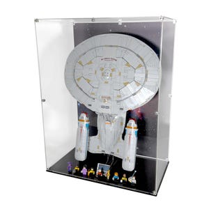 Puede incluir: Maqueta de una nave espacial en una vitrina de acrílico transparente. La nave es blanca con detalles grises y dorados, sobre un fondo estrellado. La vitrina tiene una base negra, y hay varias figuras en miniatura en la base de la nave.