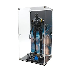 Puede incluir: Una figura LEGO K-2SO negra y gris dentro de una vitrina transparente. La figura tiene detalles amarillos y está sobre una base negra. Una figura LEGO más pequeña y un objeto azul también están en la base. El fondo presenta una escena futurista.