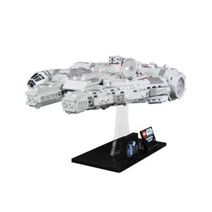 Puede incluir: Maqueta Lego gris claro del Halcón Milenario, expuesta sobre un soporte transparente con base negra. El modelo presenta detalles intrincados y una placa con el logotipo de Star Wars. Artículo de coleccionista.