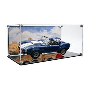 May include: A blue and white toy sports car model displayed in a clear acrylic case. The model has a white stripe down the center and is accompanied by a gold trophy and a red toolbox. The case features a desert landscape backdrop.