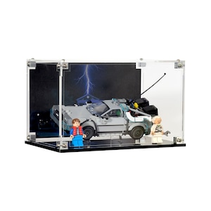 May include: A clear acrylic display case showcasing a Lego DeLorean time machine model with two Lego minifigures. The background features a lightning bolt and a house. The case is rectangular with silver hardware.