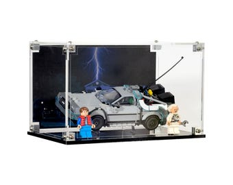 May include: A clear acrylic display case showcasing a Lego DeLorean time machine model with two Lego minifigures. The background features a lightning bolt and a house. The case is rectangular with silver hardware.