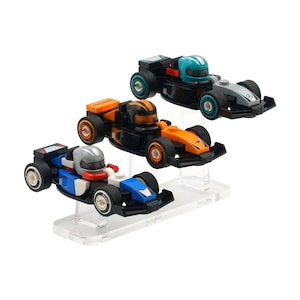 May include: Three toy race cars in blue, orange, and black, each with a driver figure. The cars are displayed on clear acrylic stands. The cars have black tires and are designed with racing details.