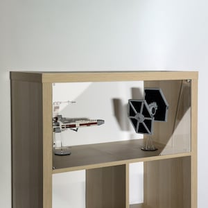May include: A light wood-tone display shelf with glass doors, showcasing two Star Wars model spaceships. One is a red and white X-wing fighter, and the other is a black TIE fighter. The shelf has multiple compartments.