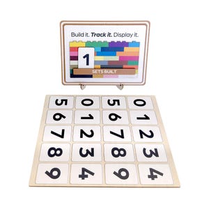 May include: A wooden display board with the text "Build it. Track it. Display it." and a colorful brick design. Below, a wooden board with numbered tiles from 0 to 9. The display shows "1 SETS BUILT".