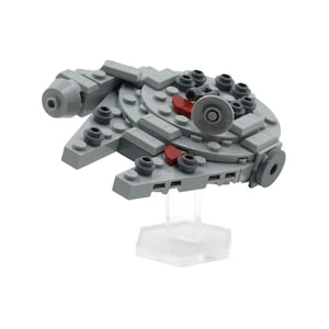 May include: A miniature gray Millennium Falcon model made of interlocking blocks. The model features a circular central section with various details, including red accents and a clear stand.