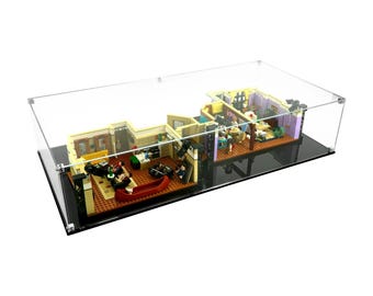 Può includere: Una teca espositiva in acrilico trasparente che mostra un dettagliato modello LEGO di un set televisivo. Il modello presenta più stanze con mobili e figure in miniatura. La teca poggia su una base nera.