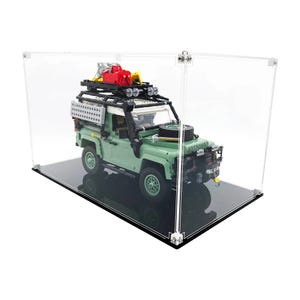May include: A green and black toy SUV model with a roof rack, spare tyre, and accessories, presented in a clear acrylic display case. The model has a white roof and sits on a black base. The case is rectangular with silver corner connectors.