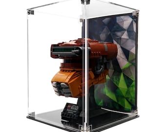 Può includere: Un modello Lego di un veicolo di Star Wars, esposto in una teca di acrilico trasparente. Il modello è principalmente arancione e marrone, con una base nera e una visiera verde. La teca ha una base nera e uno sfondo geometrico.