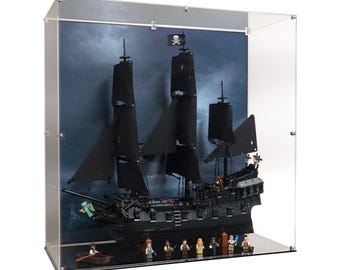 May include: A black pirate ship model with black sails and a skull and crossbones flag, displayed in a clear acrylic case. The model includes miniature figures and a small boat, set against a stormy backdrop.