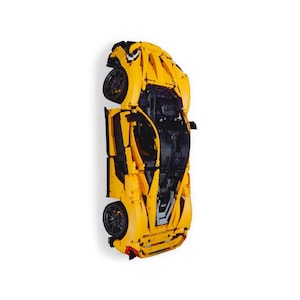 May include: A yellow and black toy sports car, constructed from interlocking plastic bricks. The model features detailed design elements, including wheels and a visible interior. The car is set against a white background, showcasing its sleek, aerodynamic form.
