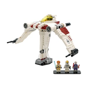以下が含まれることがあります： 黄色いコックピットを備えた白と赤のレゴスターウォーズ戦闘機モデル。モデルには2つの翼と2つの黒いブラスターがあります。3つのレゴミニフィギュアが黒いベースに立っています。
