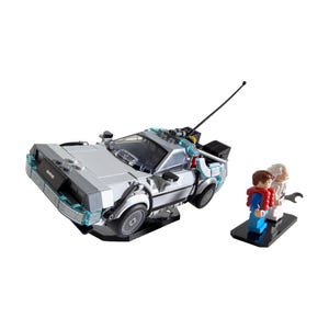 Puede incluir: Un modelo plateado del DeLorean, una máquina del tiempo, con detalles en negro y luces azules, junto con figuras en miniatura de Marty McFly y Doc Brown. El conjunto está sobre un fondo blanco.