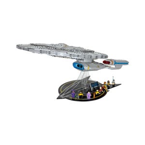 May include: A detailed model of the Star Trek USS Enterprise spaceship, constructed from interlocking building blocks. The gray ship is mounted on a black and gold display stand with miniature figures representing the crew.