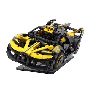 May include: A yellow and black toy car model with the text "W16" on the rear wing. The car has a sleek design with visible engine details and is displayed on a black stand. The model features a distinctive front end and wheels.
