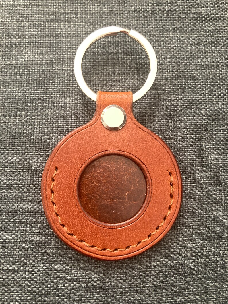 May include: A brown leather keychain with a stitched circle and a metal ring. The circle has a smaller circle cut out of the center.