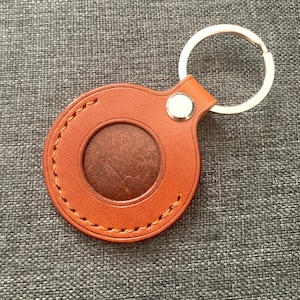 May include: A brown leather keychain with a round, stitched leather loop and a silver key ring. The loop has a circular cutout in the center.