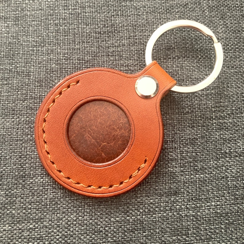 May include: A brown leather keychain with a round, stitched leather loop and a silver key ring. The loop has a circular cutout in the center.