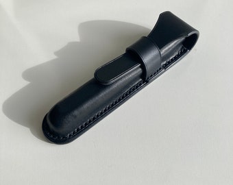 Puede incluir: Un estuche para bolígrafos de cuero negro con cierre de solapa y borde cosido.