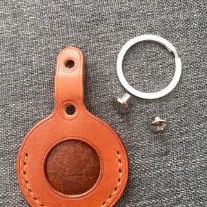 May include: A brown leather key fob with a stitched circle in the center and a metal ring attached. The key fob has two holes for attaching to a key ring.