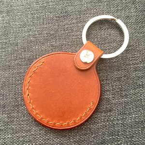 May include: A brown leather keychain with a round, stitched tag and a silver metal ring.