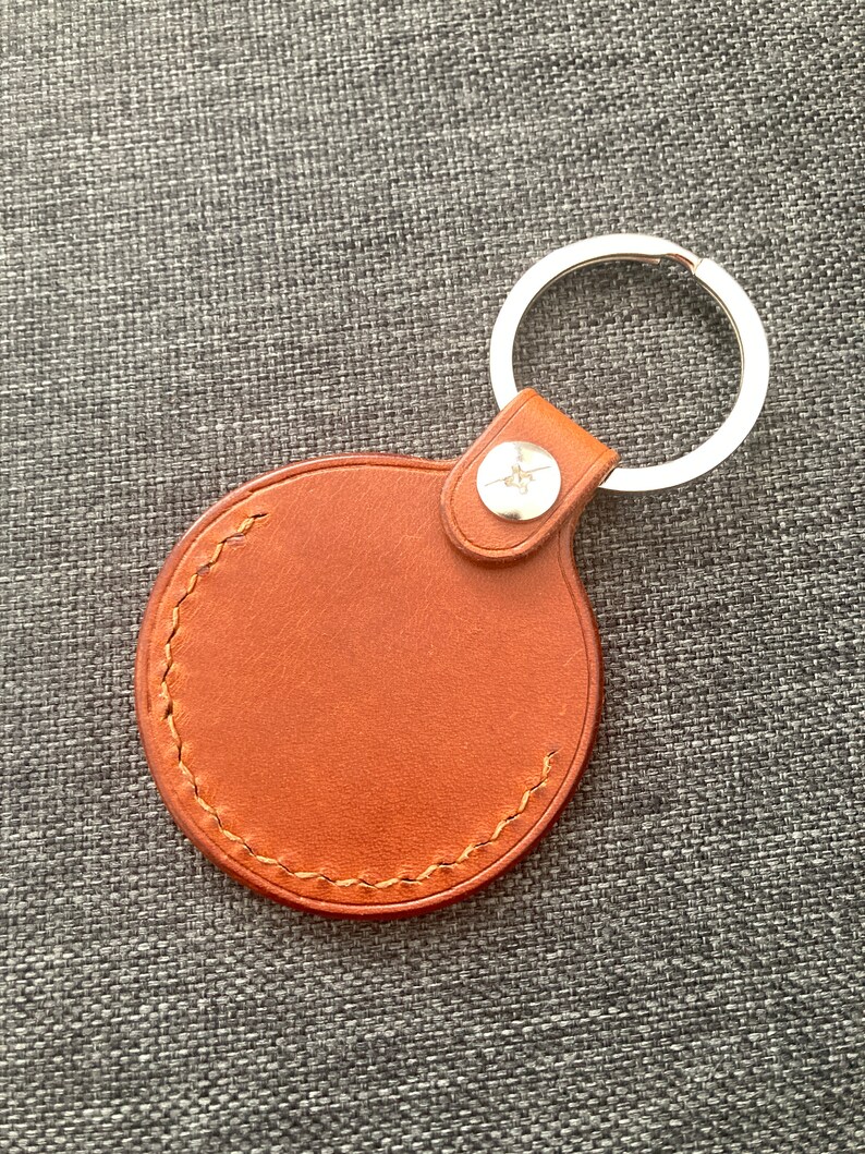May include: A brown leather keychain with a round, stitched tag and a silver metal ring.