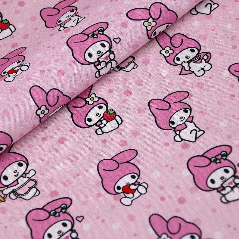 May include: Pink fabric with a repeating pattern of white cartoon rabbits with pink ears, bows, and dresses. The rabbits are holding strawberries and hearts. The background is a light pink with white polka dots.