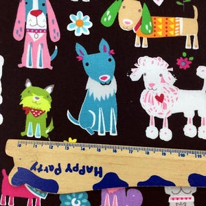 May include: A fabric with a repeating pattern of cartoon dogs in various colors, including pink, blue, green, and tan, on a dark brown background. The dogs have different designs and accessories. A wooden ruler with the text "Happy Party" is at the bottom.
