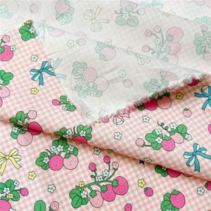 Peut inclure: Tissu rose et blanc &agrave; carreaux vichy avec un motif r&eacute;p&eacute;t&eacute; de fraises, de feuilles vertes et de petites fleurs blanches. Le tissu pr&eacute;sente &eacute;galement des n&oelig;uds bleus et jaunes. Le tissu est superpos&eacute;, montrant les deux c&ocirc;t&eacute;s.