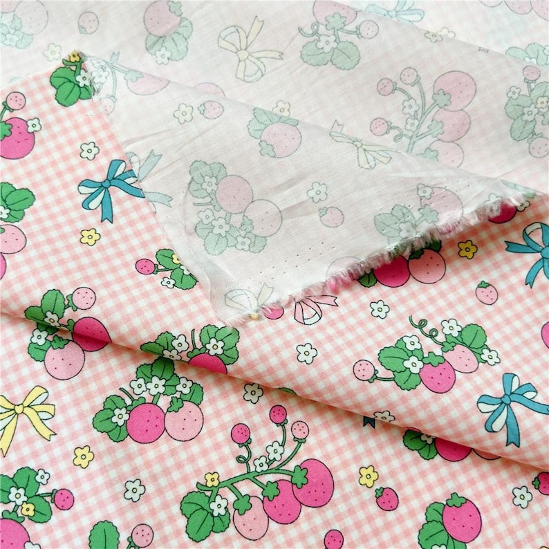 Peut inclure: Tissu rose et blanc &agrave; carreaux vichy avec un motif r&eacute;p&eacute;t&eacute; de fraises, de feuilles vertes et de petites fleurs blanches. Le tissu pr&eacute;sente &eacute;galement des n&oelig;uds bleus et jaunes. Le tissu est superpos&eacute;, montrant les deux c&ocirc;t&eacute;s.