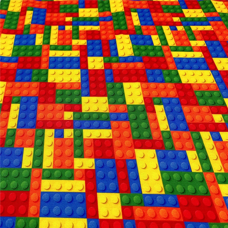 K&ouml;nnte beinhalten: Ein farbenfroher Stoff mit einem sich wiederholenden Muster aus roten, gelben, blauen, gr&uuml;nen und orangen Quadraten, die an Spielzeugbausteine erinnern.