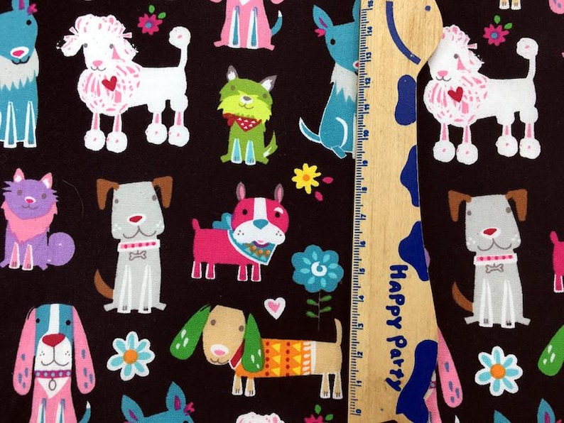 May include: A black fabric featuring a repeating pattern of colorful cartoon dogs, flowers, and hearts. The dogs are in various poses and colors, including pink, blue, green, and gray. A wooden ruler with blue and white accents is in the image.