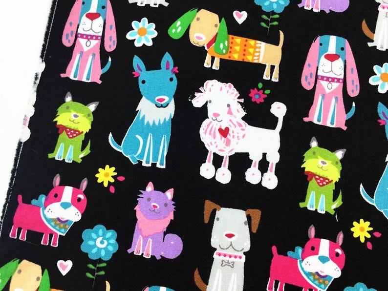 May include: Black fabric featuring a repeating pattern of colorful cartoon dogs, cats, and flowers. The dogs are depicted in various poses and colors, including pink, blue, green, and white. The cats are purple. The flowers are yellow and blue.